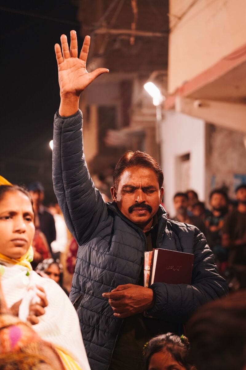 A man holding an Urdu Bible with his hand raised